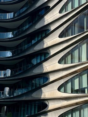 Curving, layered facade of a modern building with large windows, featuring shades of gray and blue.