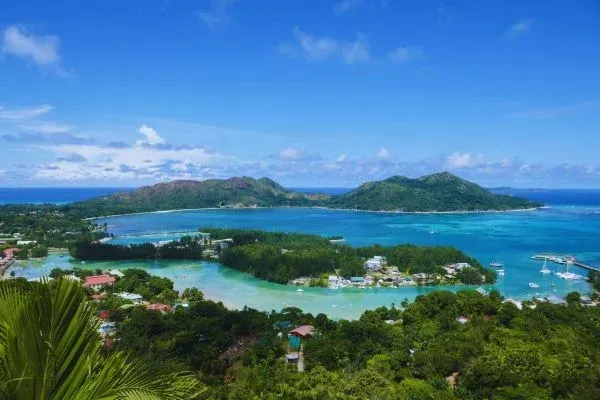 A scenic view of Seychelles with turquoise water, lush green islands, and a bright blue sky.