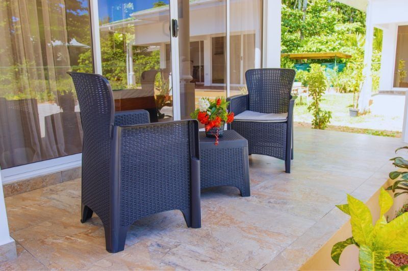 Two black wicker chairs and a small table with flowers on a tiled patio.