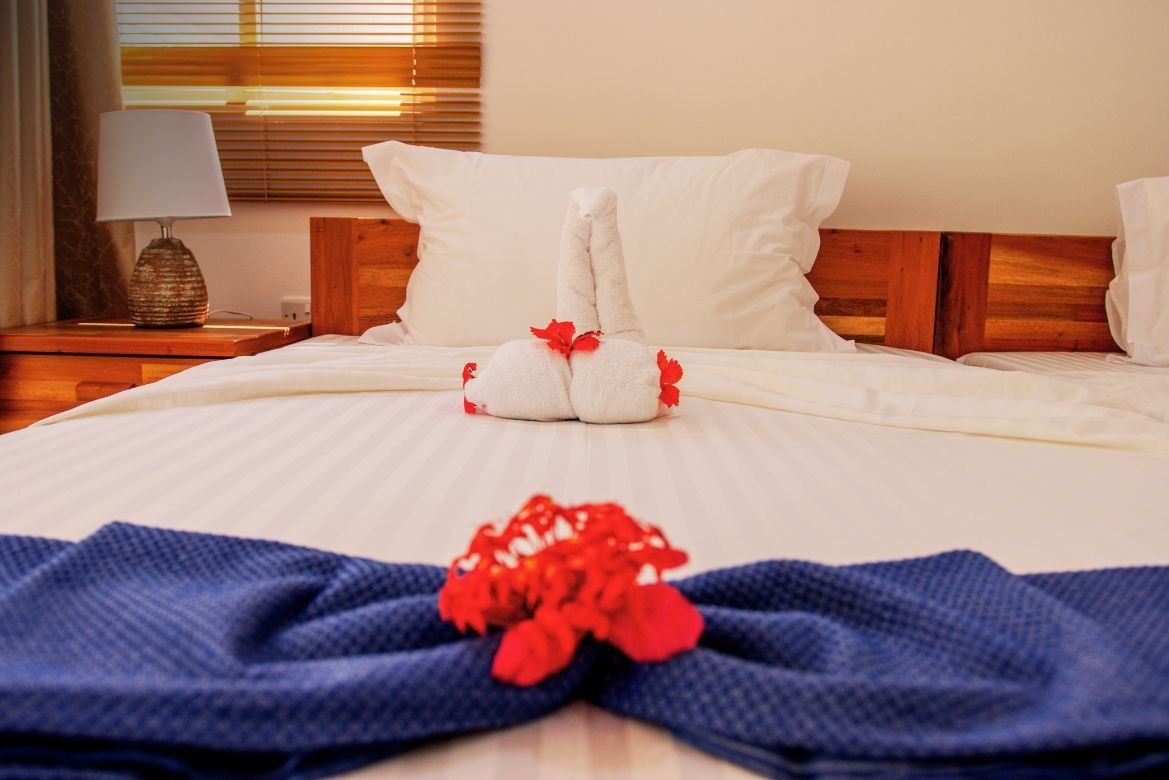 A hotel bed with a folded towel swan and blue towels arranged in a bow, decorated with a red flower.