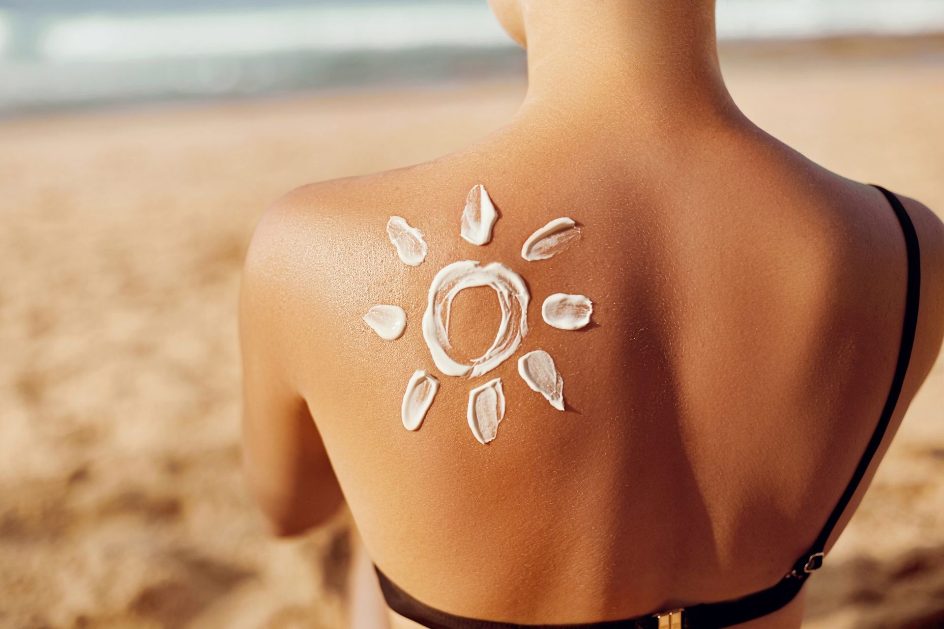 A woman is sitting on the beach with sunscreen on her back.