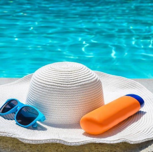 A hat, sunglasses and a bottle of sunscreen are sitting next to a pool