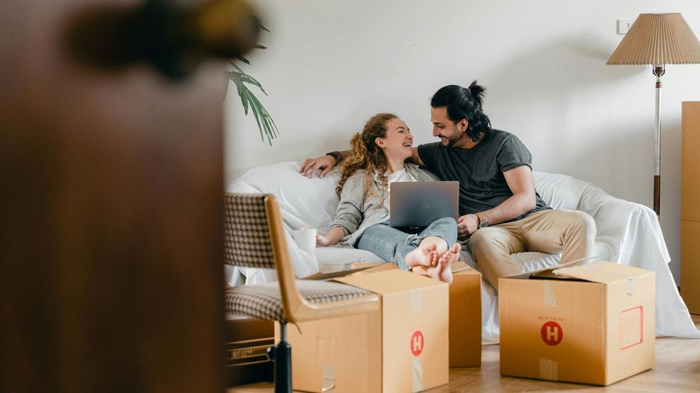 A man and a woman are sitting on a couch with boxes and a laptop.