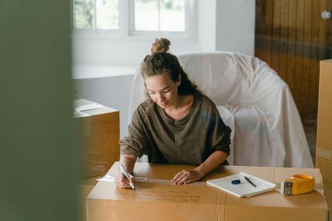 A woman is sitting at a table with boxes and writing on a piece of paper.
