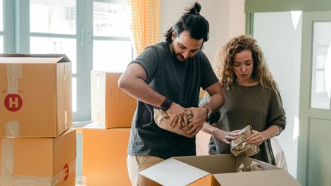 A man and a woman are packing boxes in a living room.