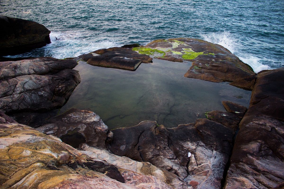 Uma piscina de água cercada por rochas no meio do oceano