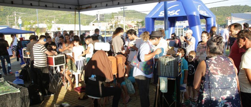 Um grande grupo de pessoas está reunido sob uma tenda azul.