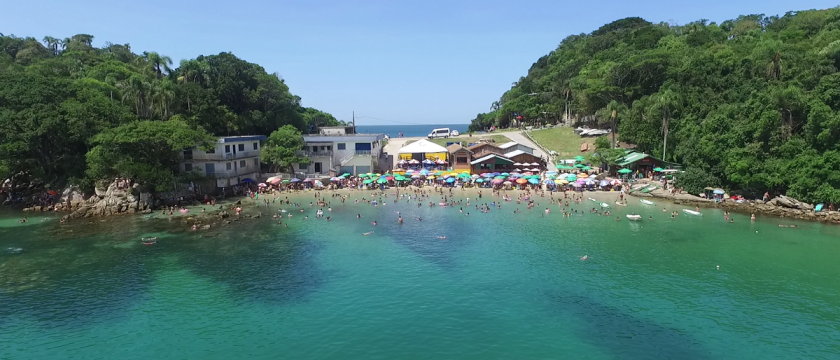 Uma vista aérea de uma praia com muita gente nadando na água.