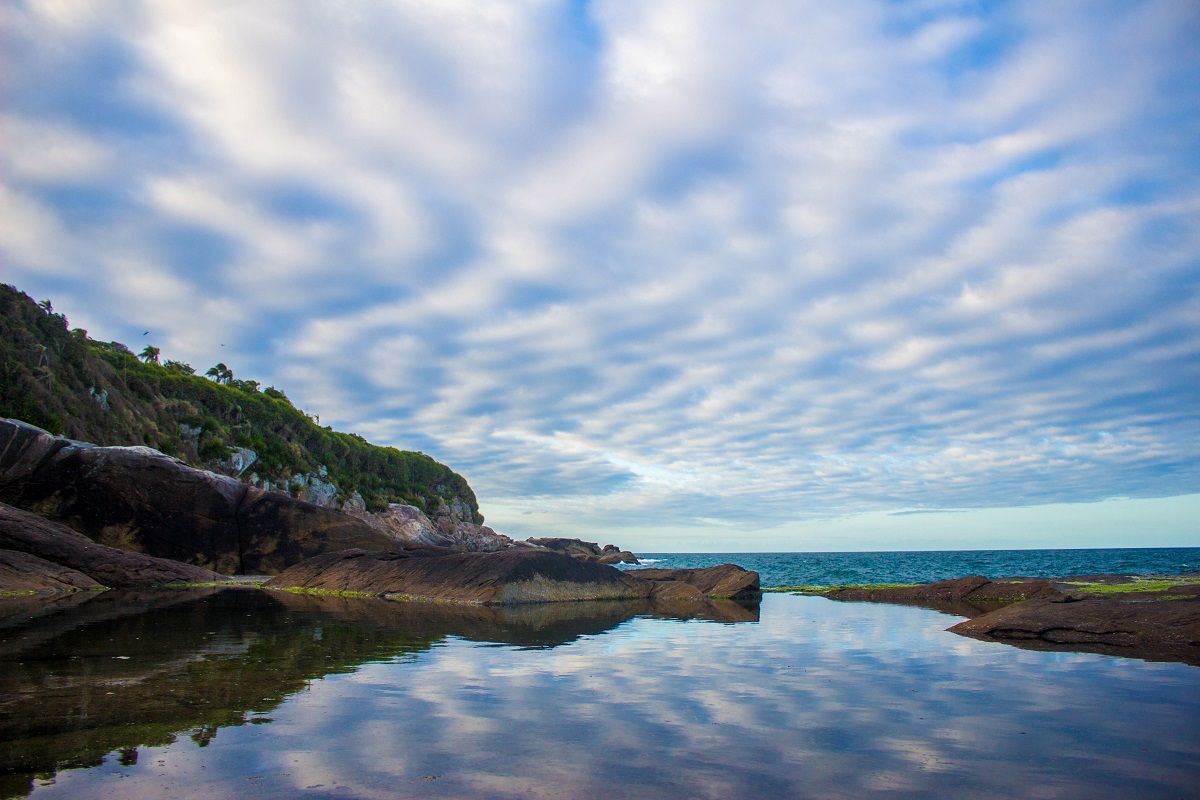 Um corpo de água cercado por pedras e árvores com um céu nublado ao fundo.