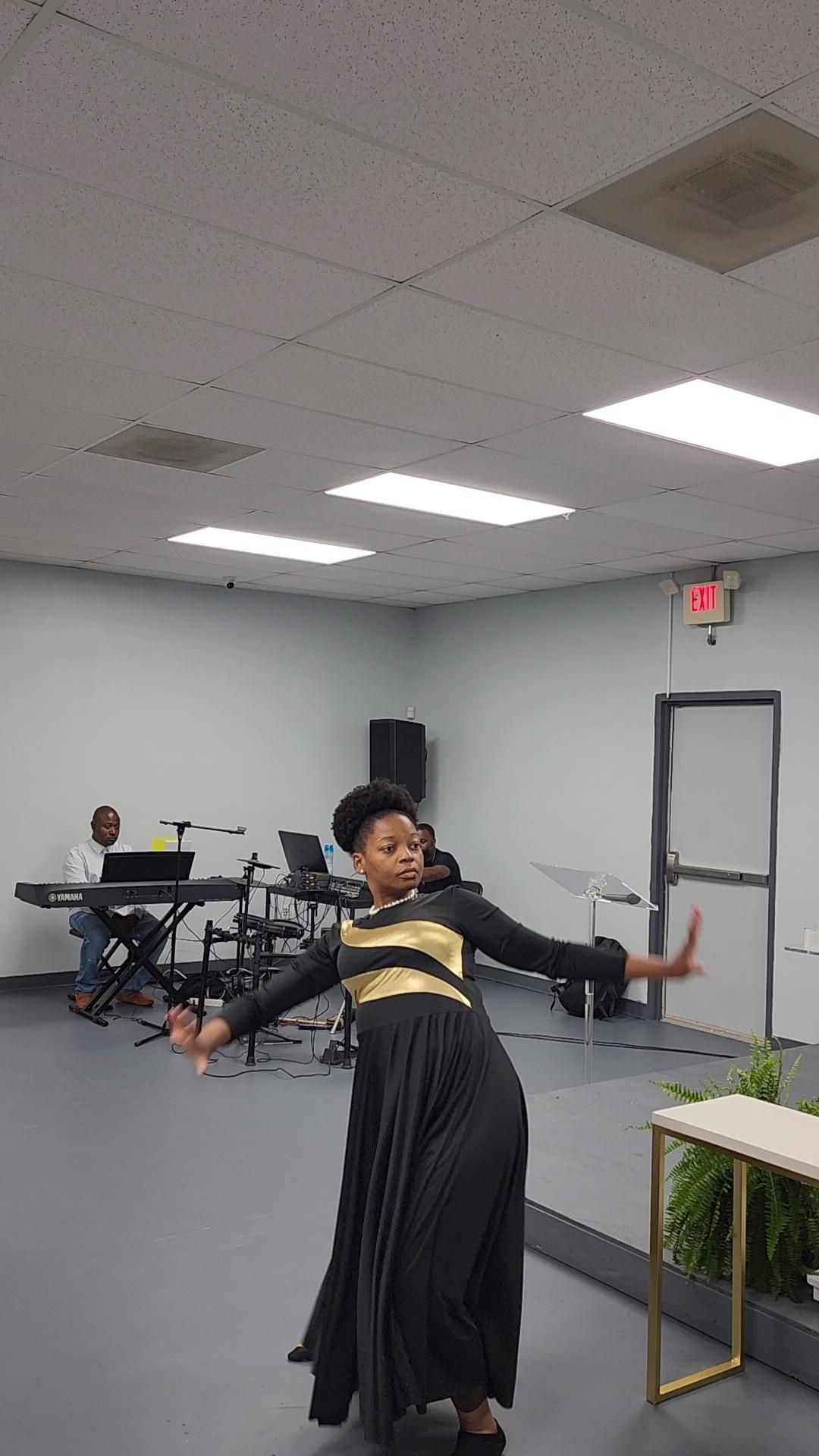 Woman in gold and black dress dancing in a room with a band in the background.