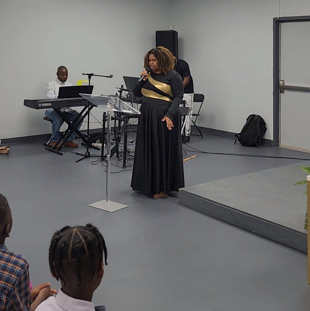 Woman in black gown singing at church, band playing. Children watch from foreground.