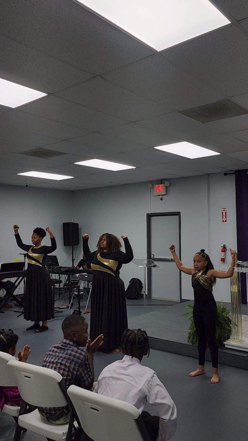 Dancers on a stage, performing in black and gold outfits. Audience claps. Church setting.