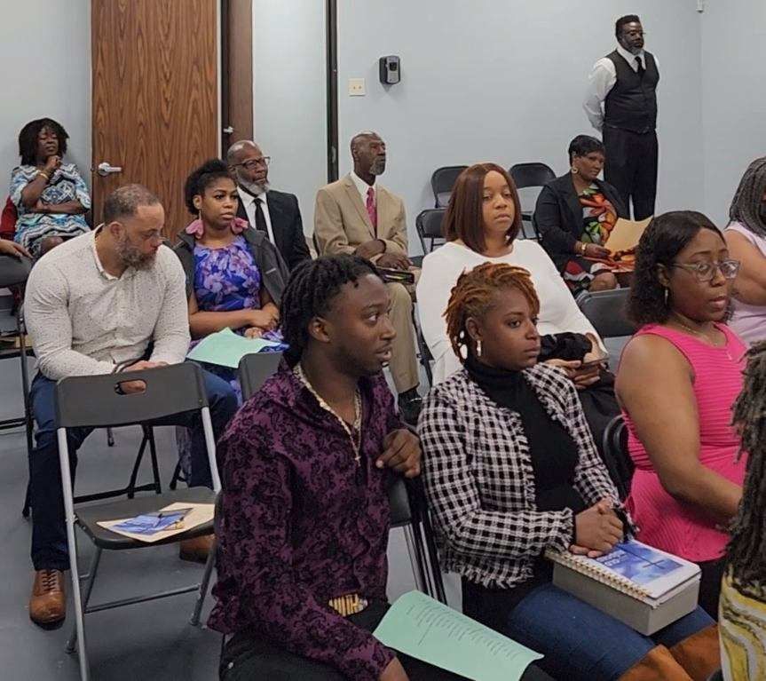 People seated in an office setting, listening attentively to a presentation. Various clothing styles and expressions.