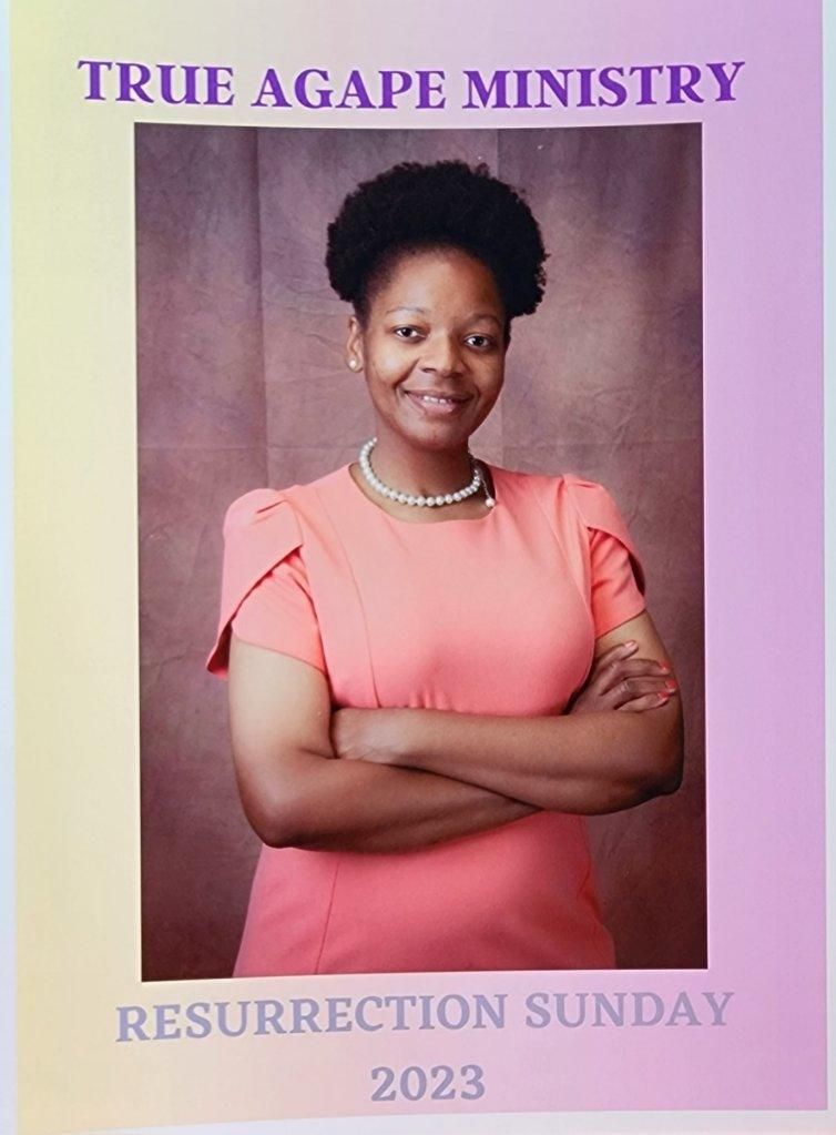 Woman in pink dress, arms crossed, smiling. 