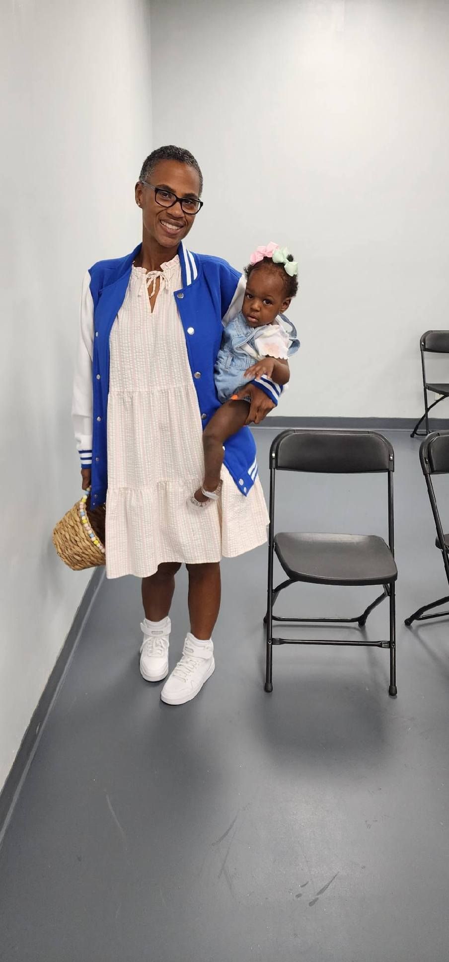 Woman in blue jacket holds a baby. They are in a room with a chair.