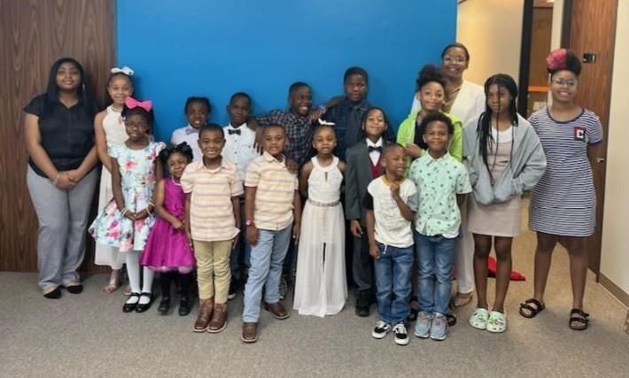 Group of children and adults smiling, posing in front of a blue wall in a building.