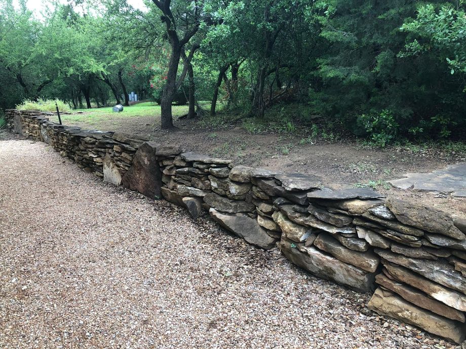 A stone wall is surrounded by gravel and trees in a park.