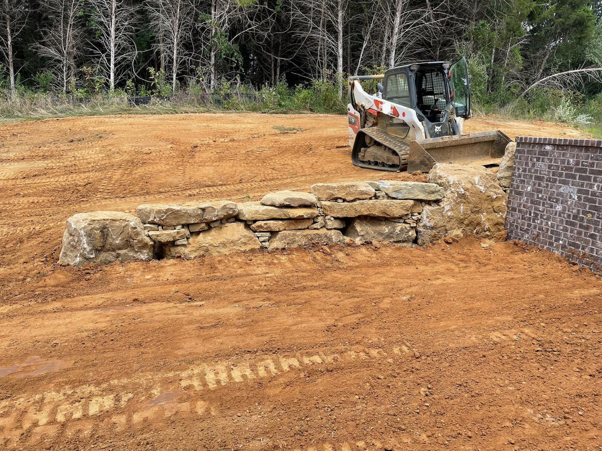 A bulldozer is moving dirt in a field next to a stone wall.