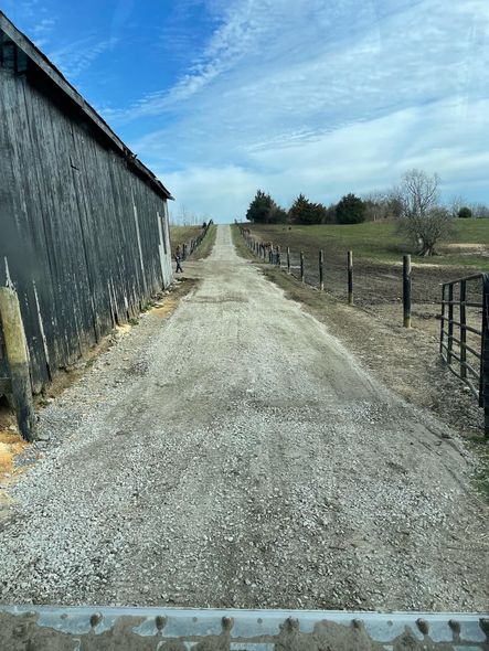 A dirt road leading to a barn in the middle of a field.