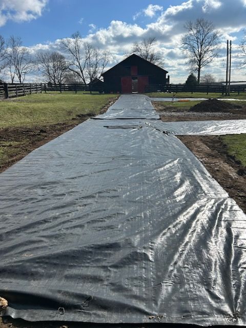 A black tarp is covering a dirt road in front of a barn.