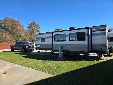 A truck hitched to a camper parked on grass at a campsite, under a blue sky.