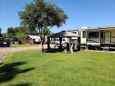 Camping scene: RV next to a grassy area with a gazebo and tree. A dog sits under the gazebo.