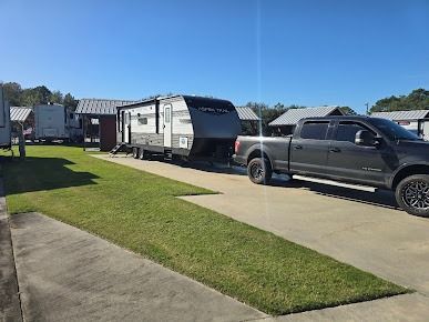 A travel trailer hitched to a truck parked on concrete with a grassy area at an RV park.