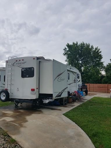 White RV parked on a concrete pad with slide-out extended, green grass, overcast sky.
