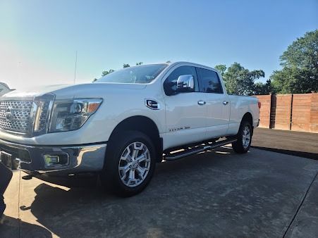 White Nissan Titan pickup truck parked on a concrete surface under a bright blue sky.