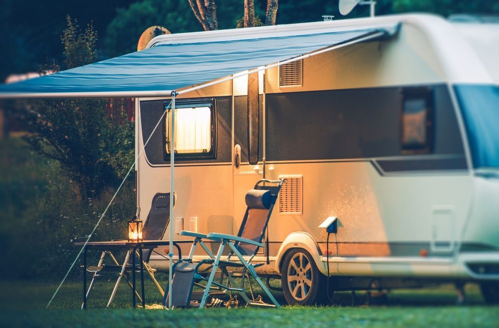 RV parked with awning extended, table, chair, and glowing lantern at night.