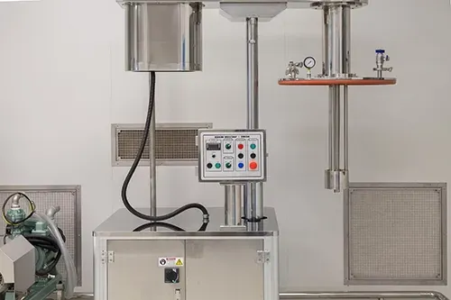 Stainless steel laboratory mixing machine with a control panel, vertical shaft, and gauge mounted against a white wall.