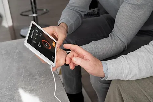 Two people sit together, one holding a white smart home display while the other points to the touchscreen interface.
