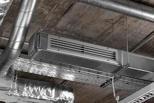 Industrial HVAC equipment and silver metallic ductwork installed on an exposed concrete ceiling.