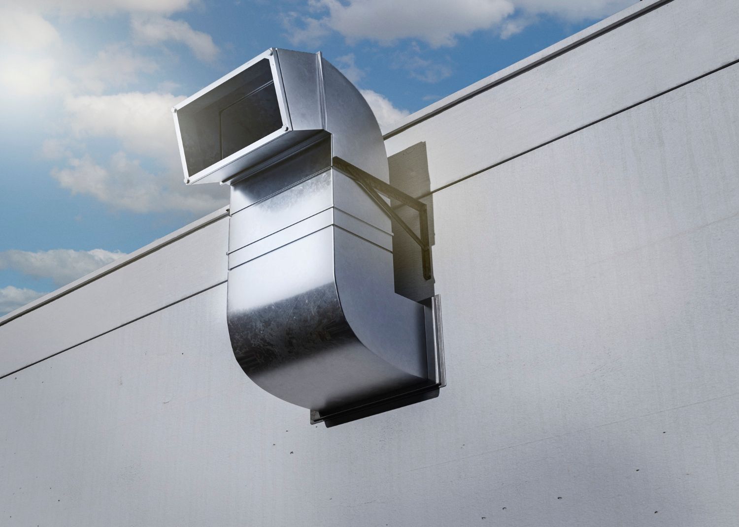 Metal ventilation duct extending from a white exterior wall against a blue sky with light clouds.