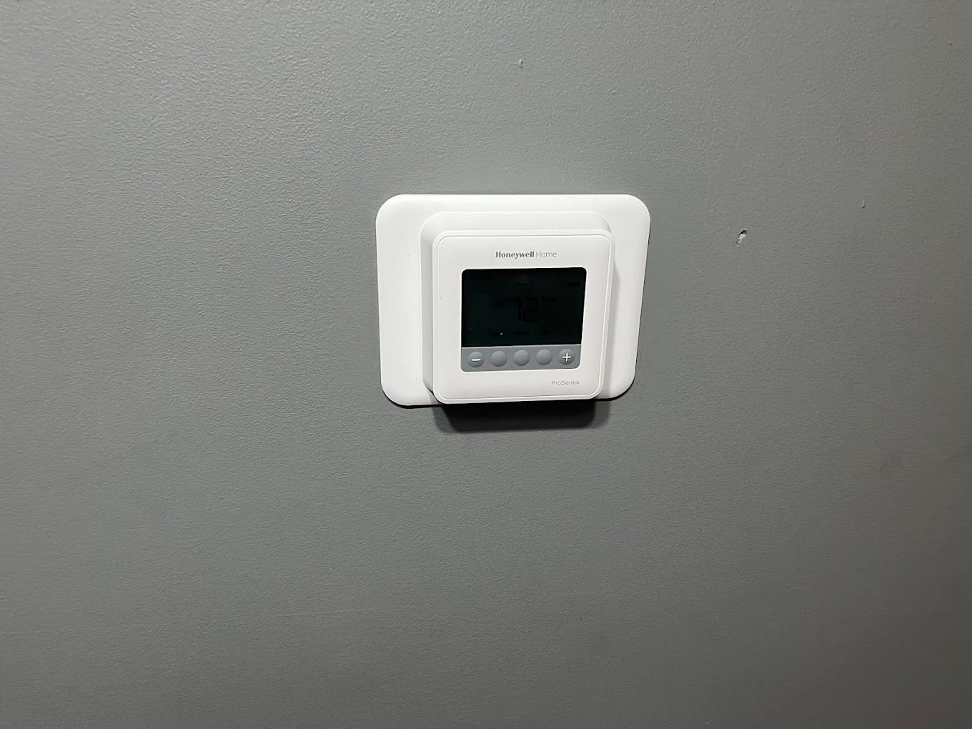 A white digital wall thermostat mounted on a grey wall.