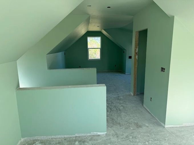 Interior of an attic-like room, painted light green, with a small window at the end.
