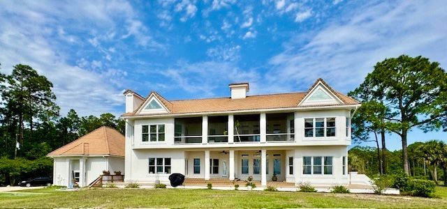 Two-story white house with screened-in porch, brown roof, and green lawn, blue sky.