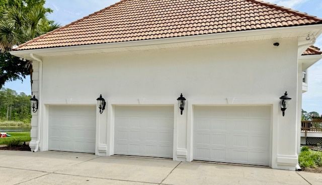 White three-car garage with matching doors, decorative lighting, and a tile roof.