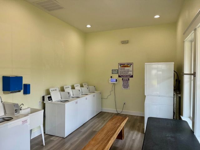 A laundry room with white appliances, a bench, and a window. Yellow walls and wood-look flooring.