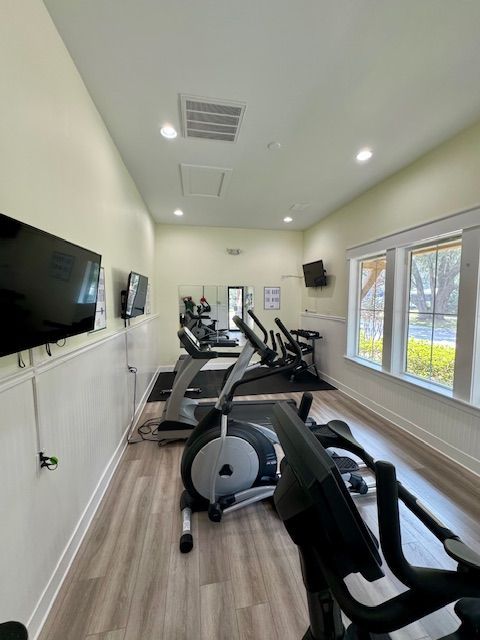 Gym with elliptical machines, treadmills, TVs, and windows, in a well-lit room.