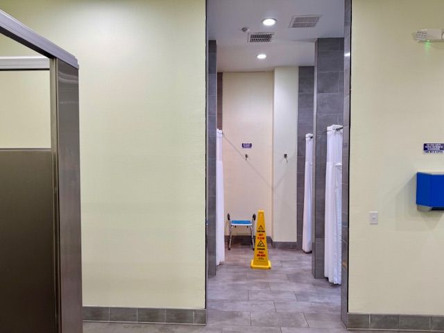 Public restroom with open stalls, a wet floor sign, and a small stool.