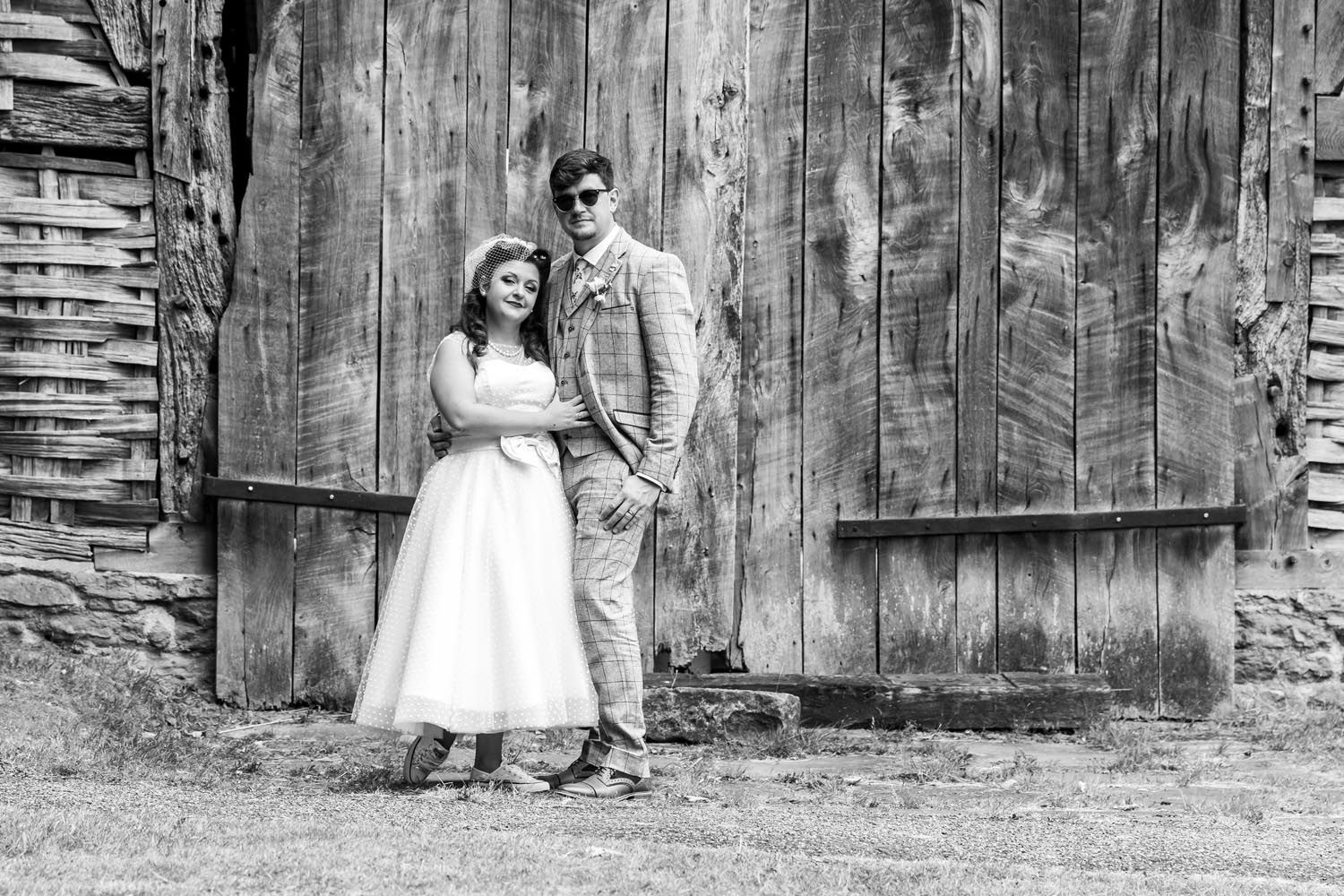 A black and white photo of a bride and groom standing in front of a wooden building.
