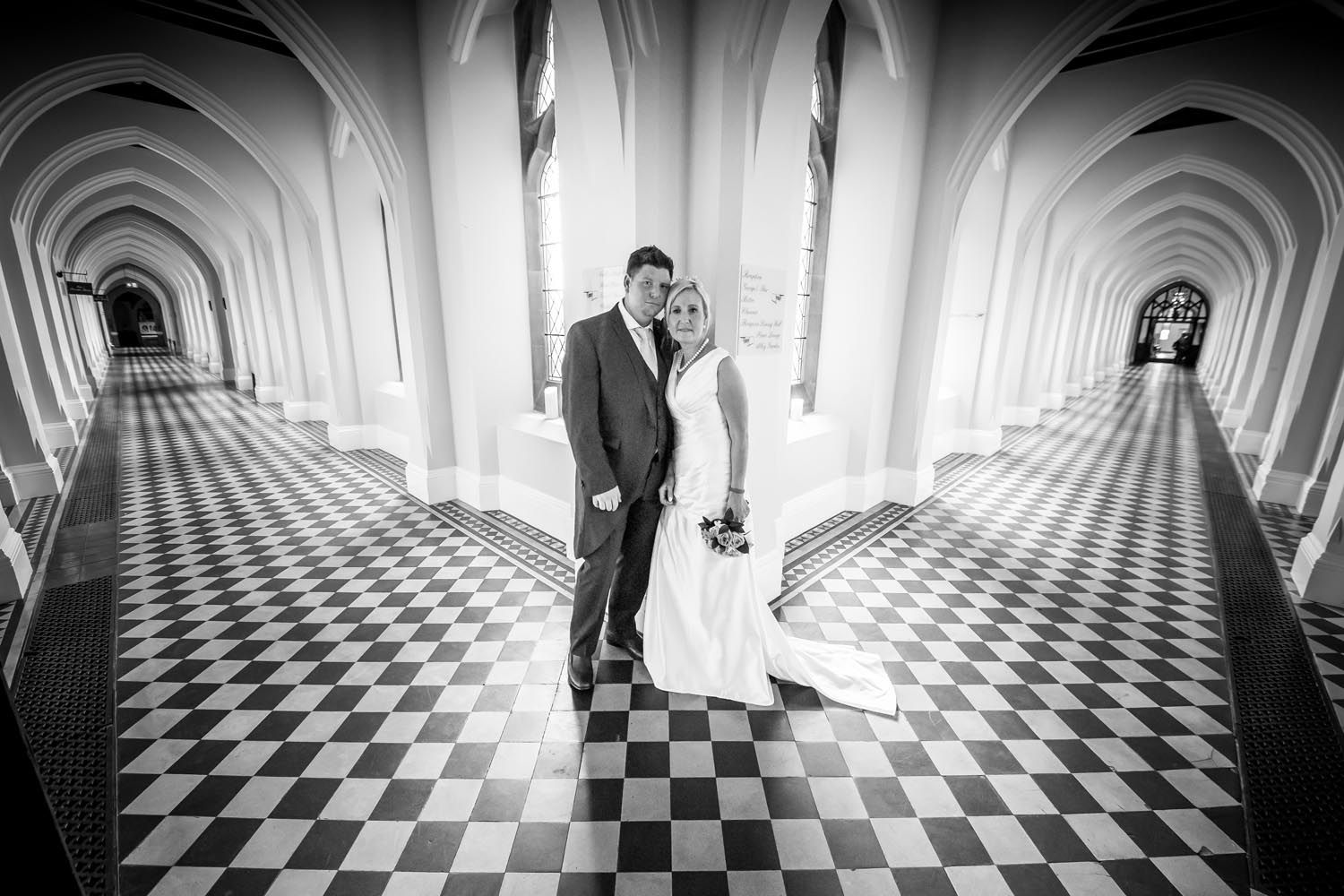 A black and white photo of a bride and groom standing in a hallway.