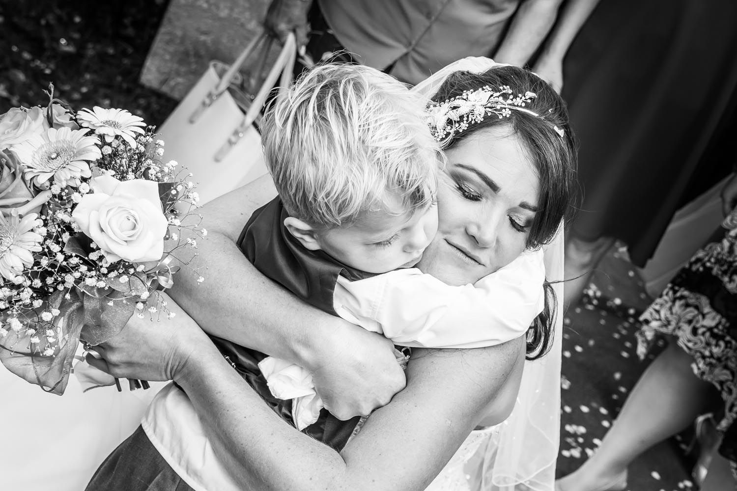 A bride is hugging a little boy at her wedding.