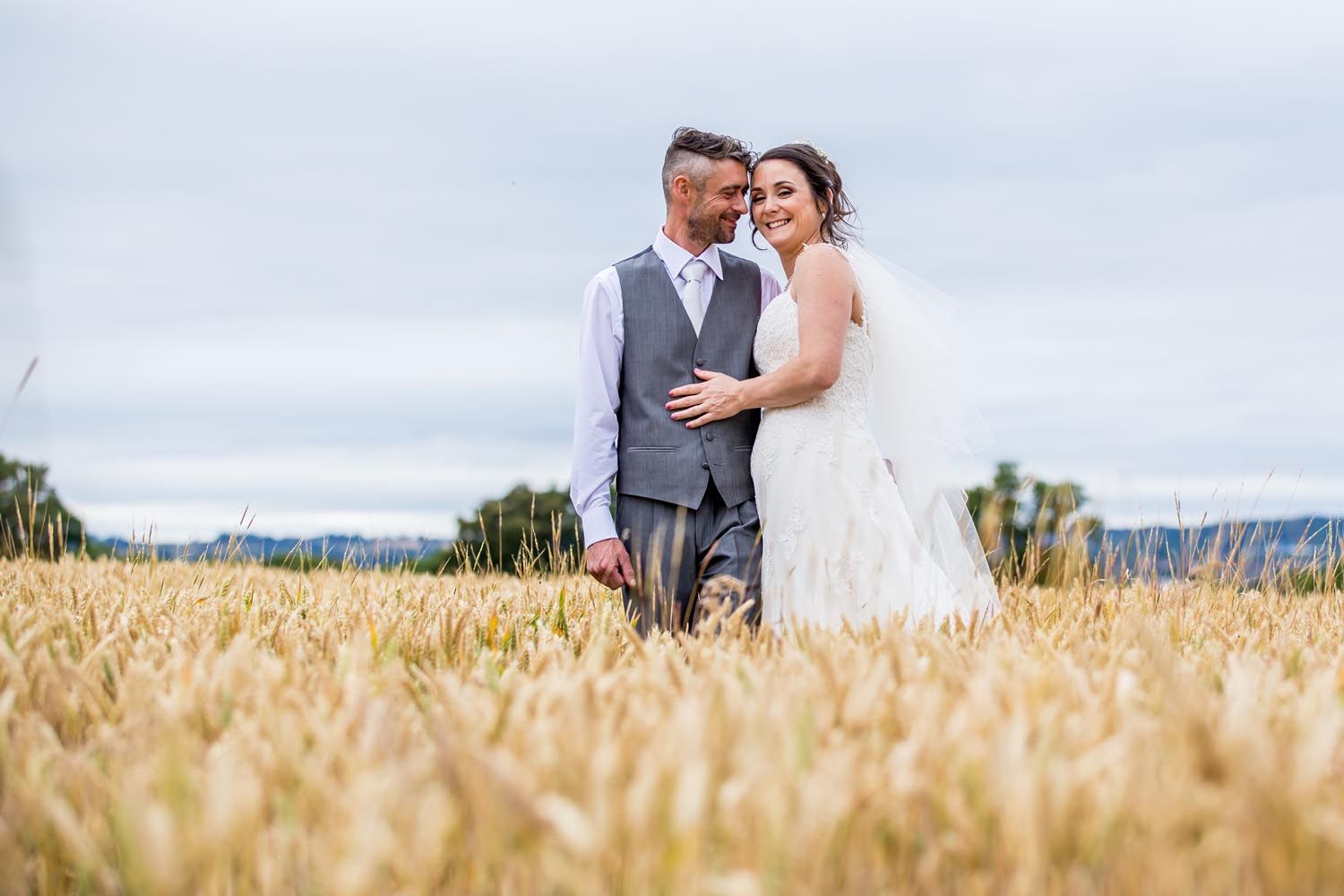 A bride and groom are standing in a field of wheat.