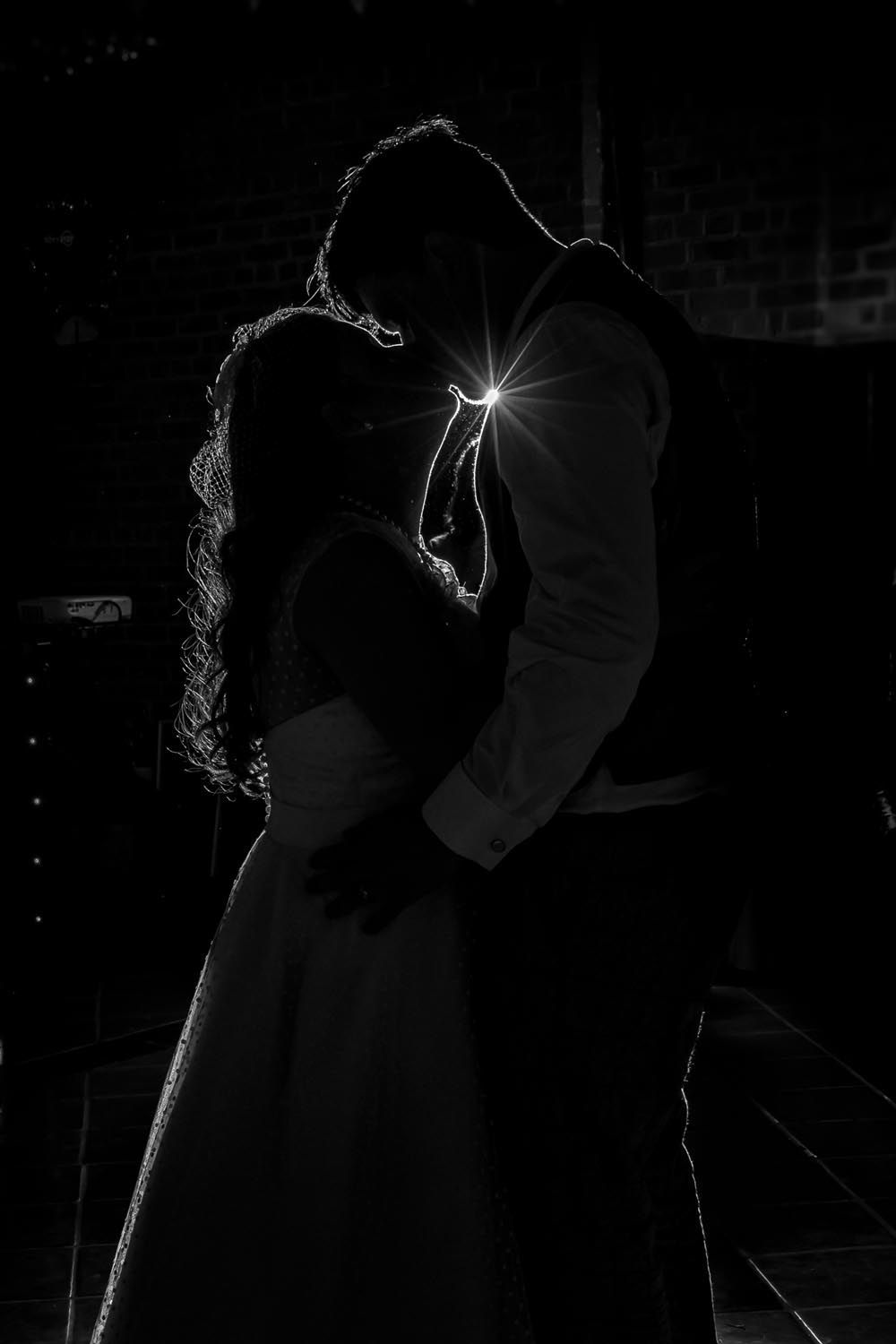 A bride and groom are dancing in the dark in a black and white photo.