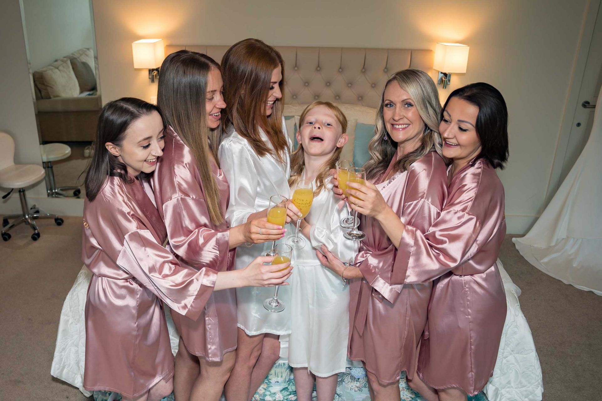 A bride and her bridesmaids are toasting with champagne in a bedroom.