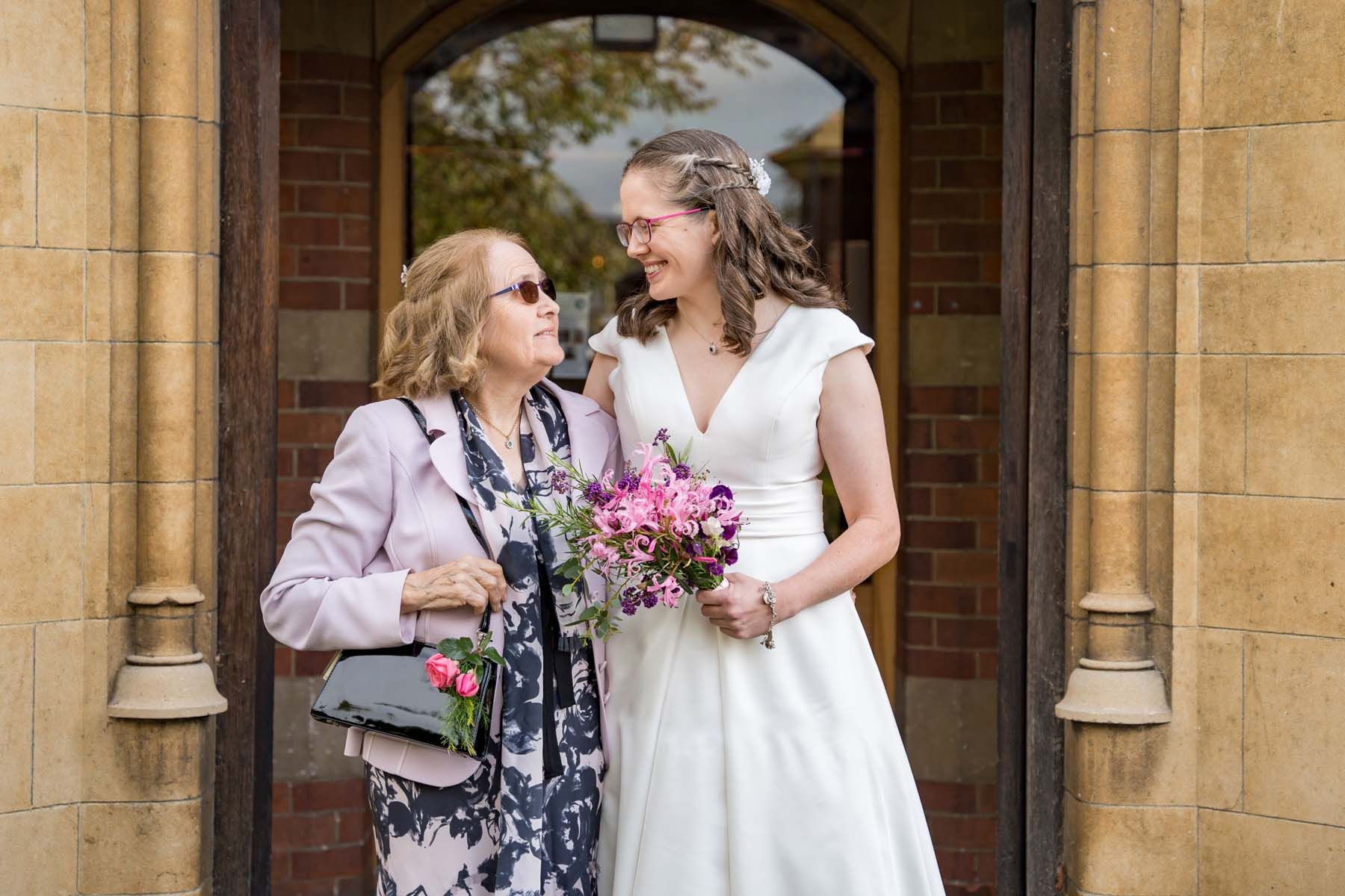 A bride and her mother are posing for a picture in front of a building.