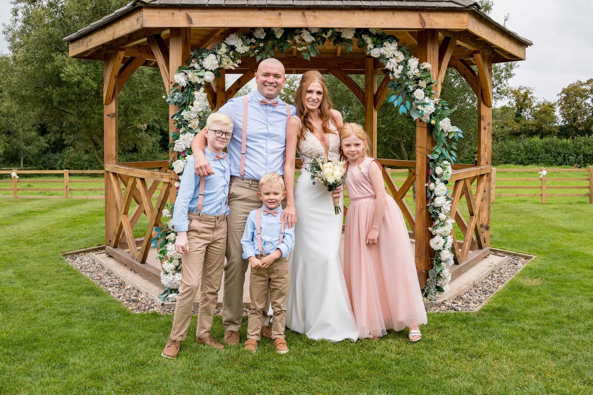 A bride and groom are posing for a picture with their children in front of a gazebo.