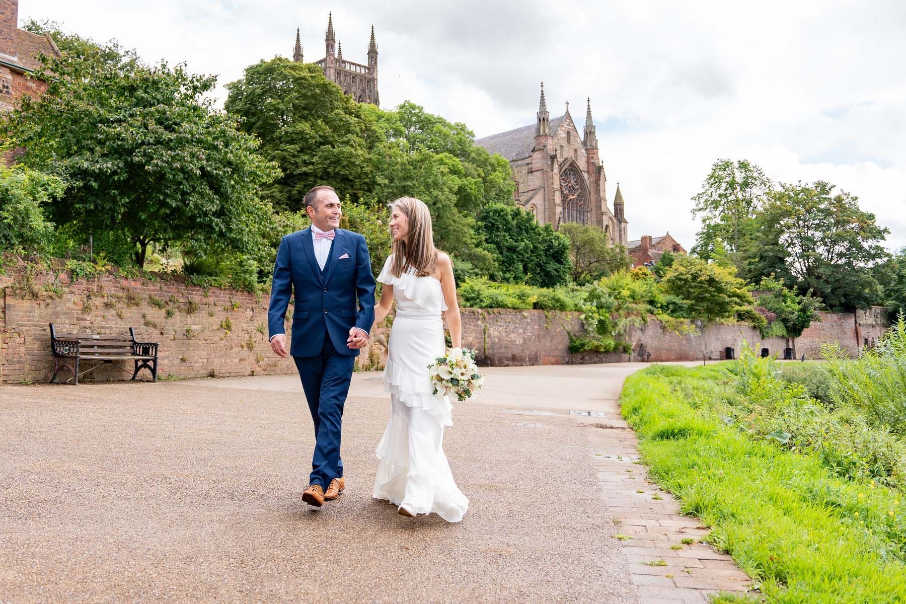 A bride and groom are walking down a path in front of a large building.